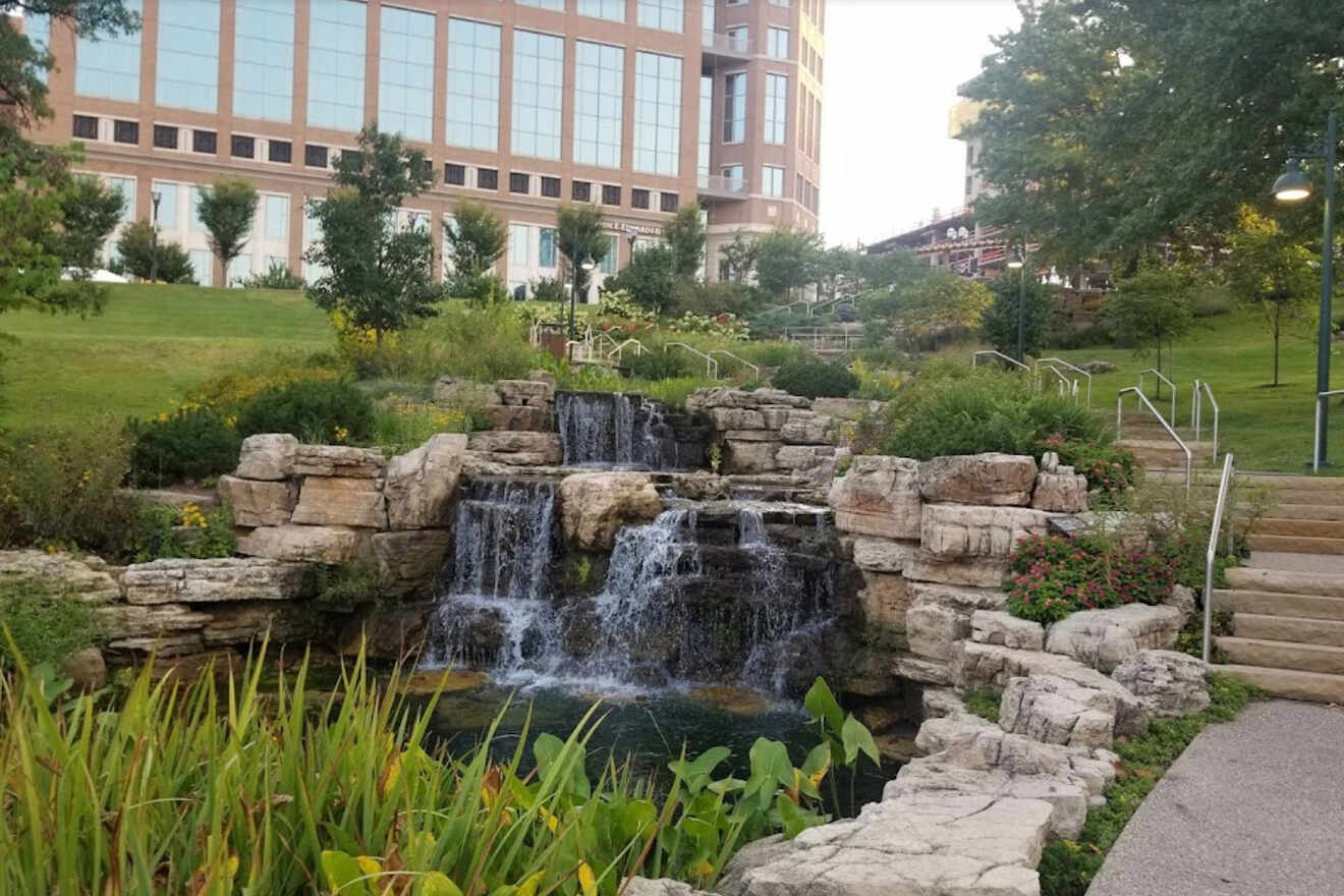 A tranquil urban park in St. Louis with a multi-tiered water feature, landscaped greenery, and a backdrop of modern buildings